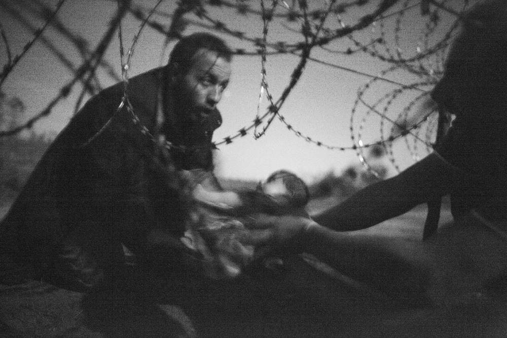 A man passes a baby through the fence at the Hungarian-Serbian border in Röszke, Hungary, 28 August 2015