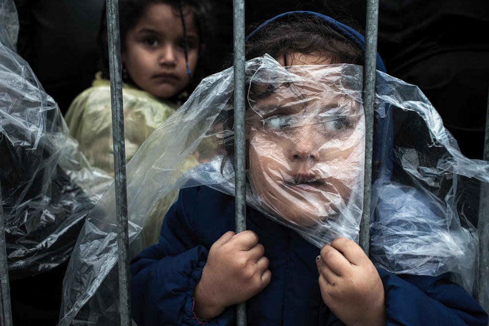 People 1st place. A child is covered with a raincoat while she waits in line to register at a refugee camp in Preševo, Serbia.