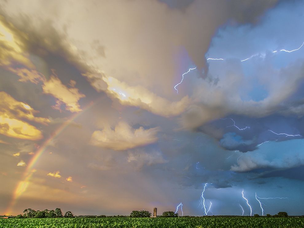 14 Warring Weather. Photograph by Paul Brooks.        "While trying to provide storm coverage for local affiliates, Iowa storm chaser Paul Brooks followed a cell from Albia to Mount Pleasant at sunset. He captured this scene just east of Mount Pleasant—lightning to the south and a well-defined rainbow to the east—by stacking seven separate shots on top of each other, forming a composite image of the weather events. “Truly a perfect alignment of the elements,” he writes.