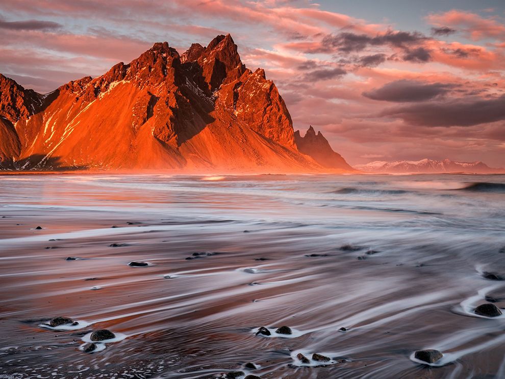 22 Planet Iceland. Photograph by Sophie Carr.     “This [was] taken at the volcanic beach at Stokksnes in southeastern Iceland in February 2015,” writes photographer Sophie Carr. “I used a two-second exposure to capture the water trails as the waves receded over rocks at the edge of the beach, just as the sun was setting behind me, illuminating the mighty Vestrahorn mountain and some peaks in the far distance.”