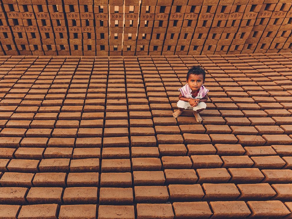 28 Brick World. Photograph by Aditya Varma.    "Bricks surround a young child in Tirupati, Andhra Pradesh, India. The country’s brick industry is particularly harsh on both its workers—who suffer dangerous conditions under much criticized labor practices—and the environment, consuming around 24 million tons of coal annually."
