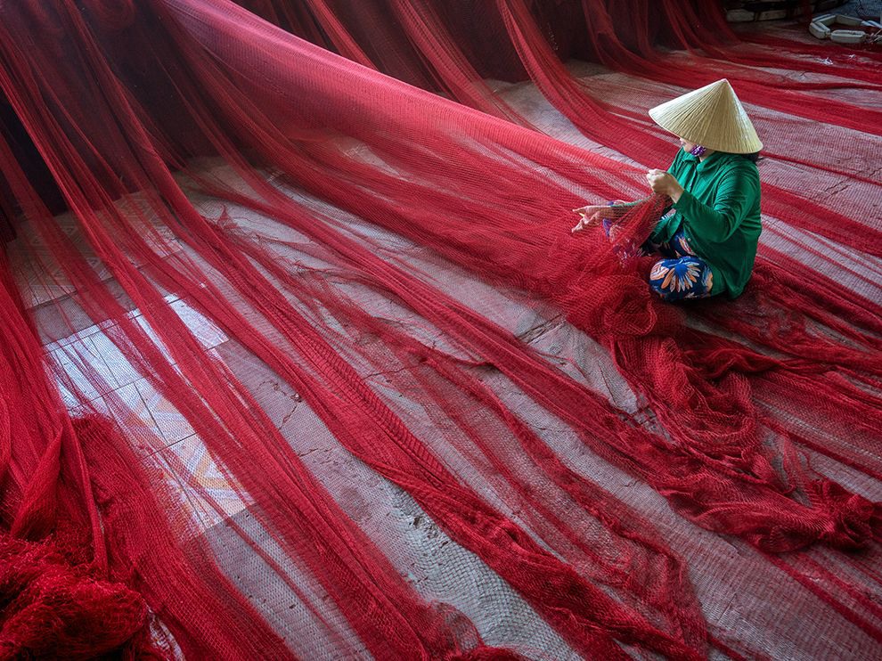 31 "Make and Mend". Photograph by Phạm Tỵ. In the Mekong Delta town of My Tho, Vietnam, a flowing expanse of fishing net is carefully checked for damage.